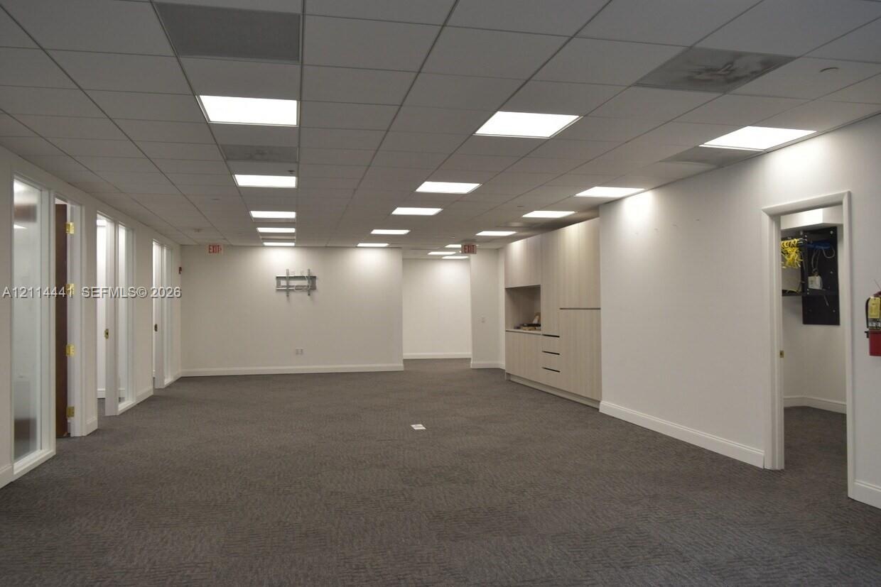 Open-concept floor plan featuring a grid ceiling with recessed panel lighting, neutral carpeting, built-in cabinetry, and glass-paneled interior doors