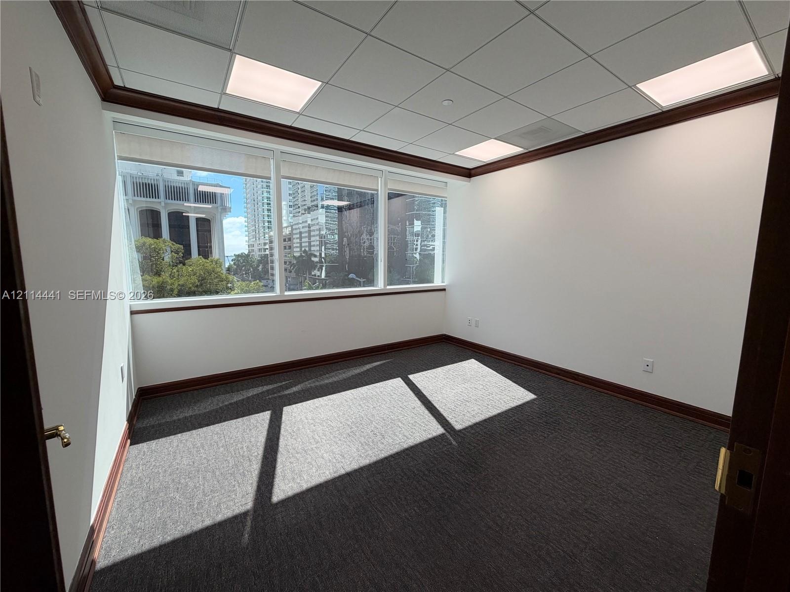 Enclosed space featuring expansive windows, dark carpeting, integrated drop ceiling panels, and wood-finish crown molding