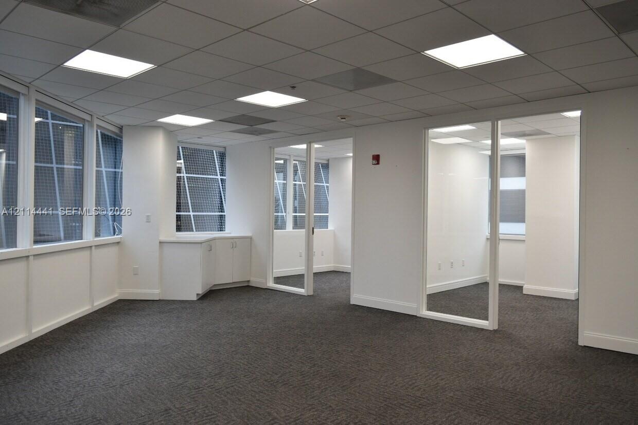 Expansive workspace featuring large windows with grid detailing, built-in lower cabinetry, a drop ceiling with integrated recessed lighting, and glass