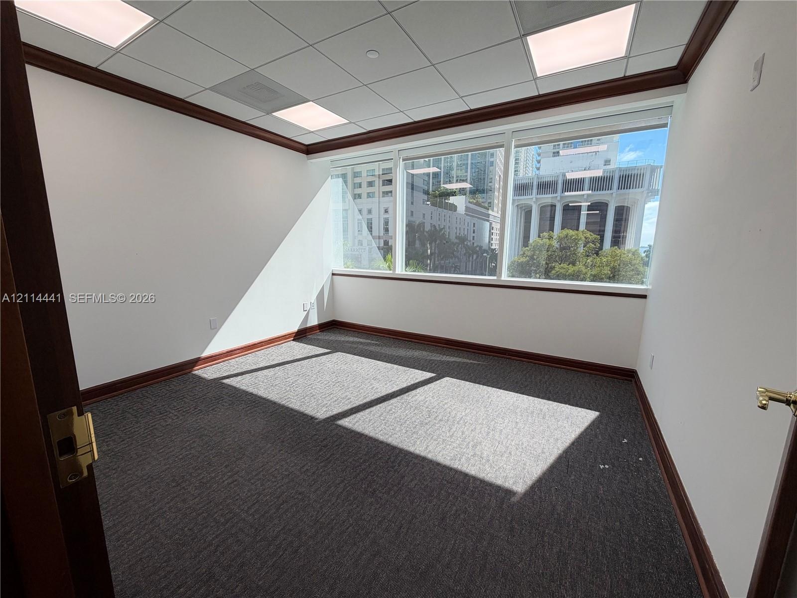 Office space featuring floor-to-ceiling windows, dark-tone carpeting, suspended grid ceiling panels, recessed lighting, and dark wood-finish crown mol