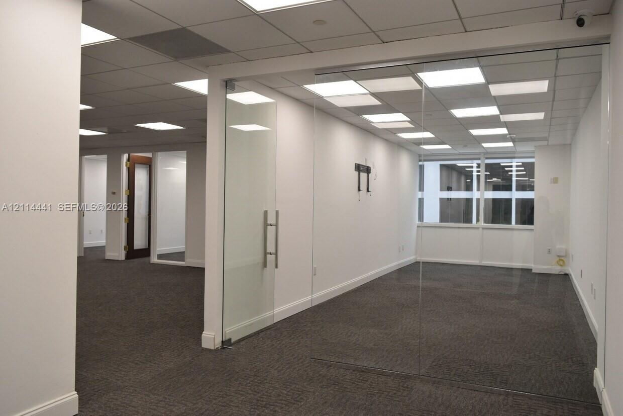 Interior space featuring floor-to-ceiling glass wall partitions, a frameless glass entry door with stainless steel hardware, drop ceiling with recesse