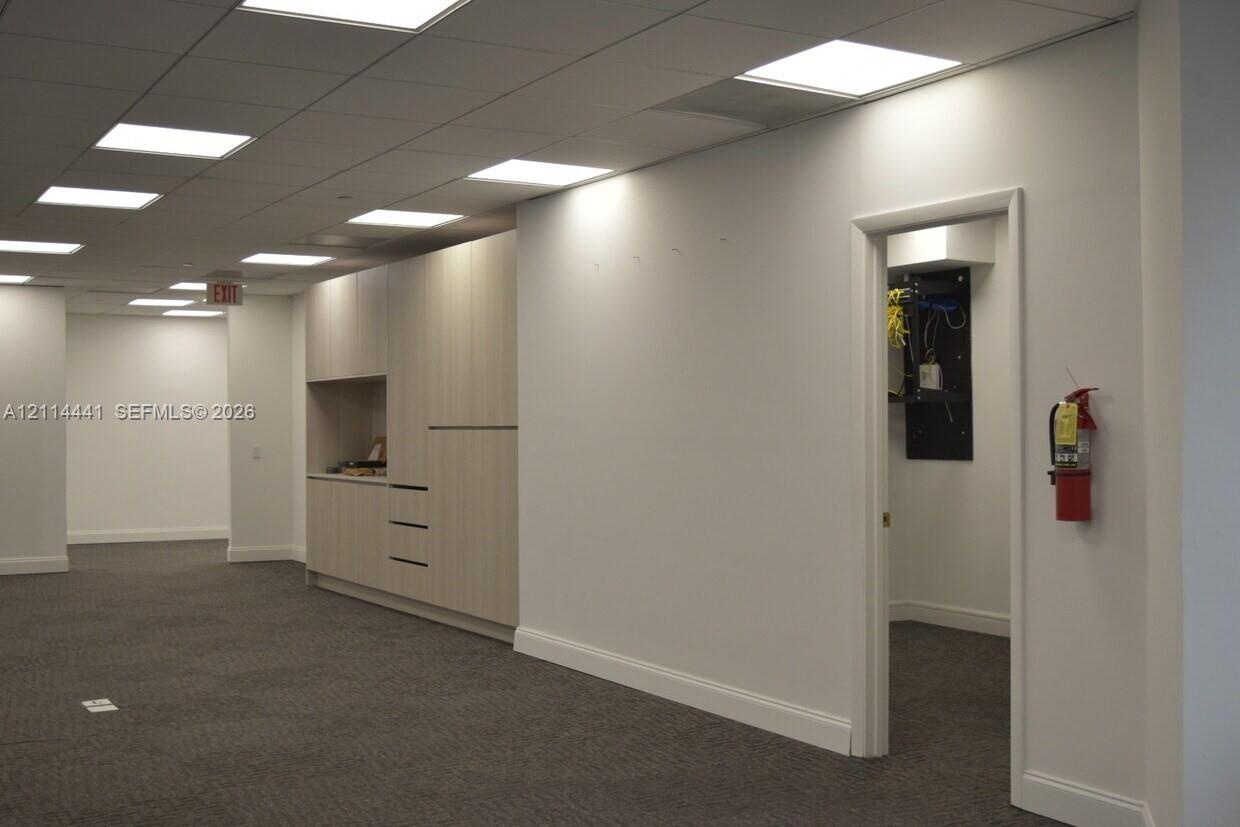 Expansive open-plan area featuring a drop ceiling with recessed panel lighting, neutral-toned carpeting, built-in light-finish cabinetry with integrat