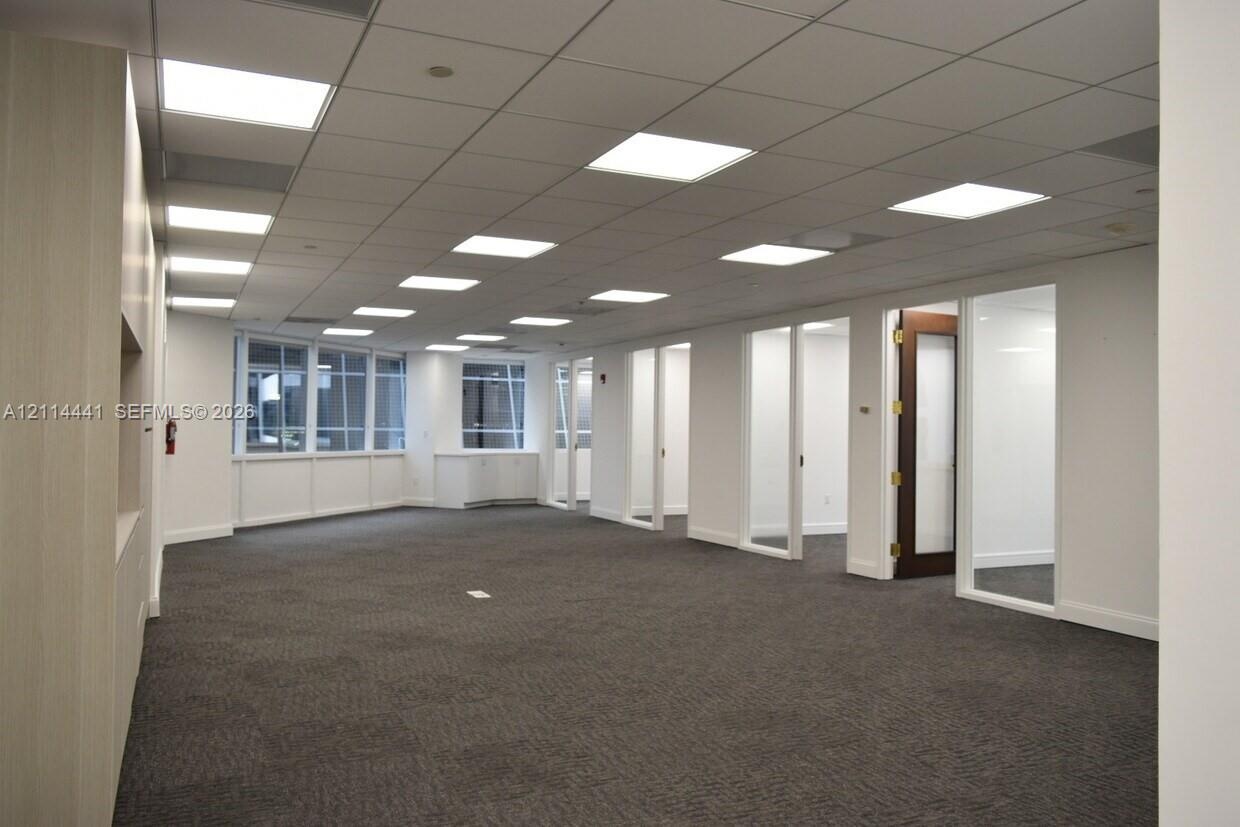Open-concept interior featuring a grid-pattern drop ceiling with recessed LED lighting, wall-to-wall carpeting, multiple glass-paneled entryways, and 