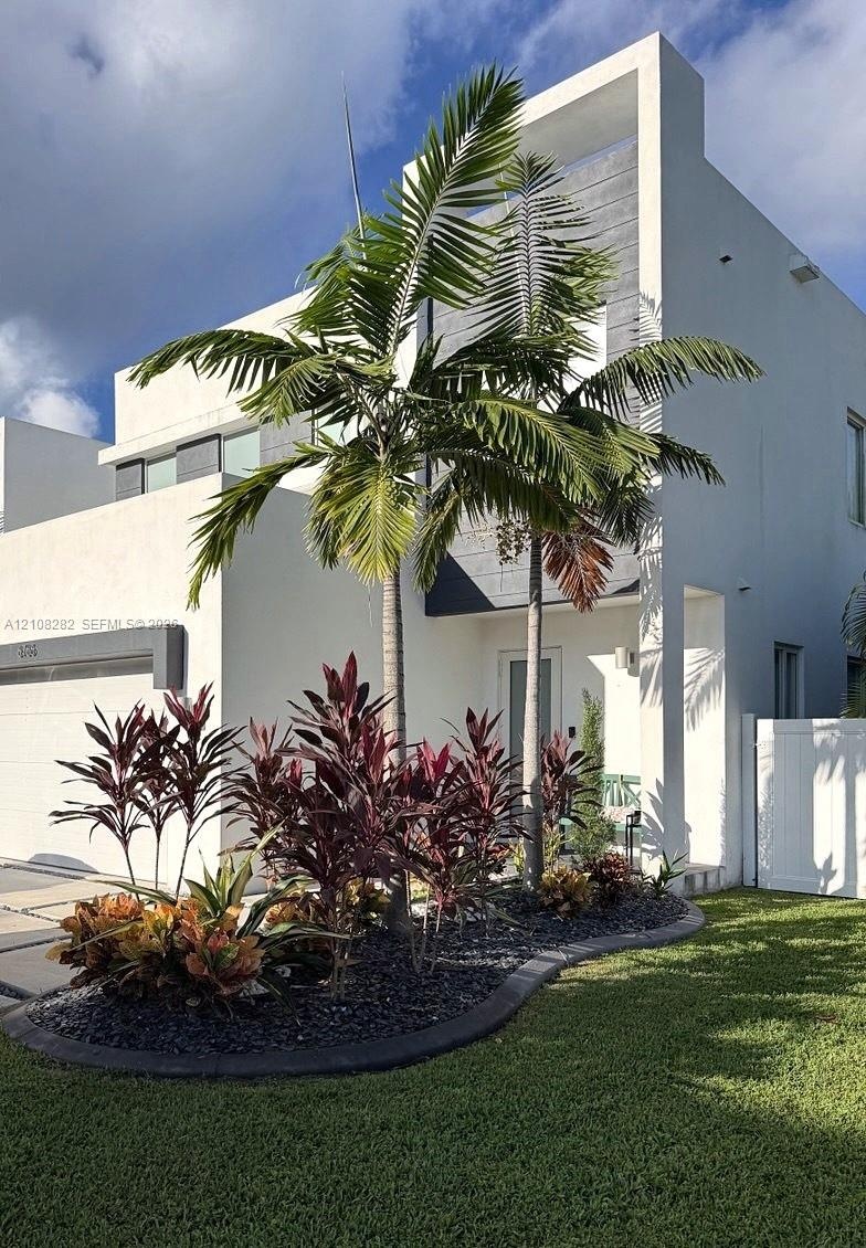 Modern contemporary exterior featuring clean white stucco siding, a recessed entryway, an integrated garage, and curated landscaping with mature palm 