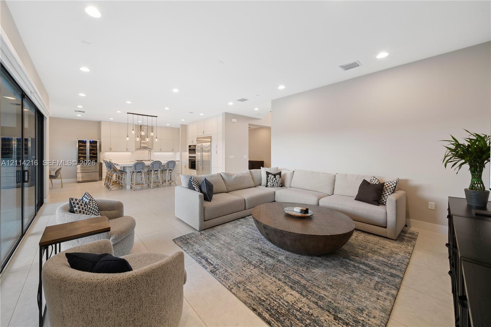 Open-concept interior featuring large-format tile flooring, recessed ceiling lighting, sliding glass doors, and a kitchen equipped with a center islan