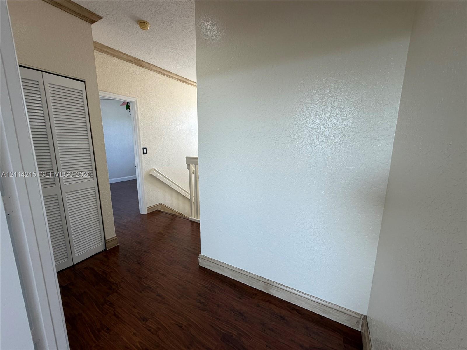 Wood-finish flooring, white louvered closet doors, textured wall finishes, and a staircase with a wooden handrail and balusters