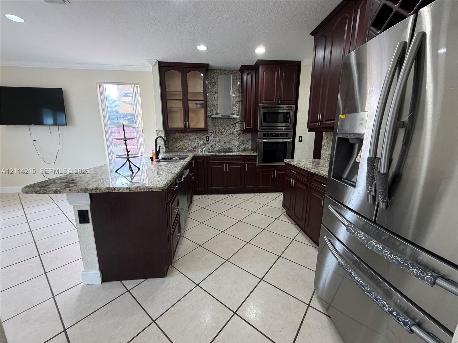 Kitchen featuring dark wood cabinetry, stone-surface countertops, stainless steel appliances, a central island, and recessed lighting