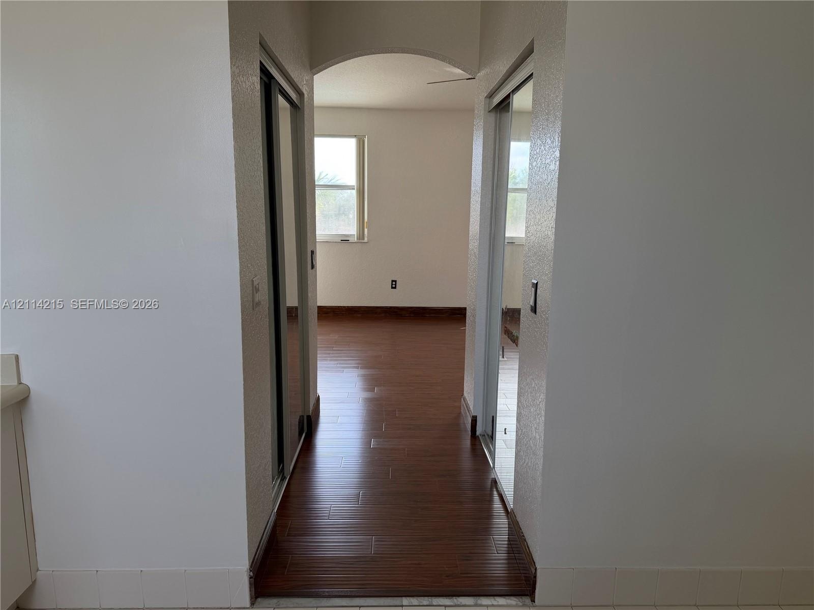 Arched hallway featuring wood-finish flooring and dual mirrored sliding closet doors