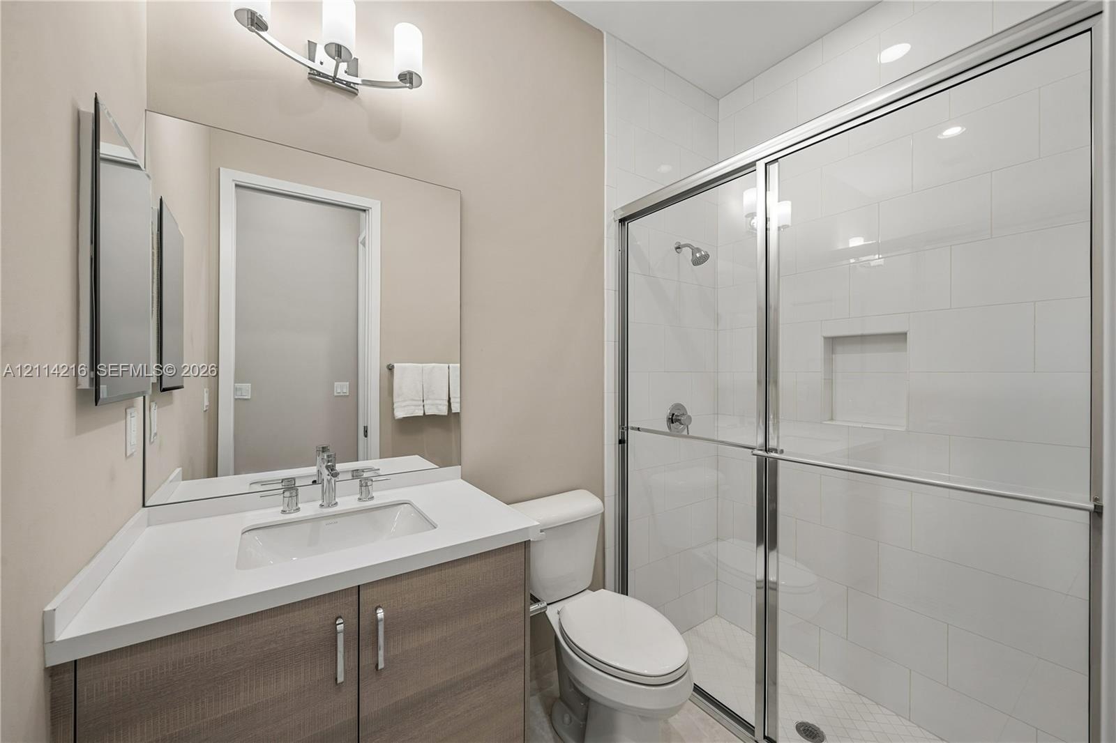 Bathroom featuring a wood-finish vanity with a stone countertop, an integrated rectangular sink, a glass-enclosed shower with subway tile surround, an