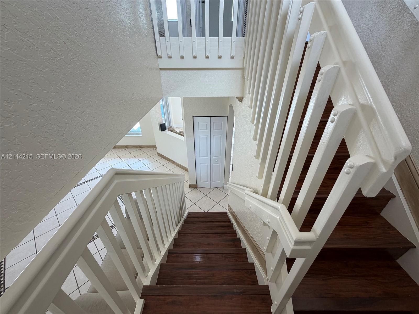 Staircase featuring wood-finish treads and white balusters with matching handrails, complemented by ceramic tile flooring and white bi-fold closet doo