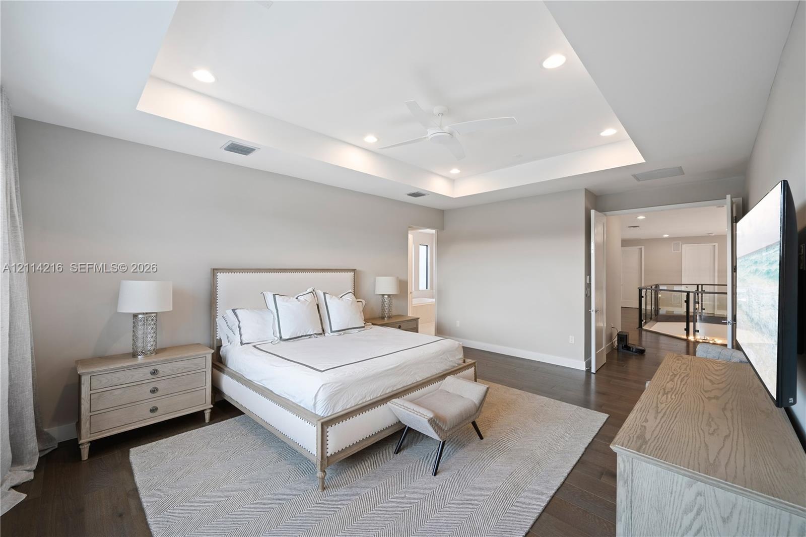 Tray ceiling with recessed lighting, central ceiling fan, and dark wood-finish flooring