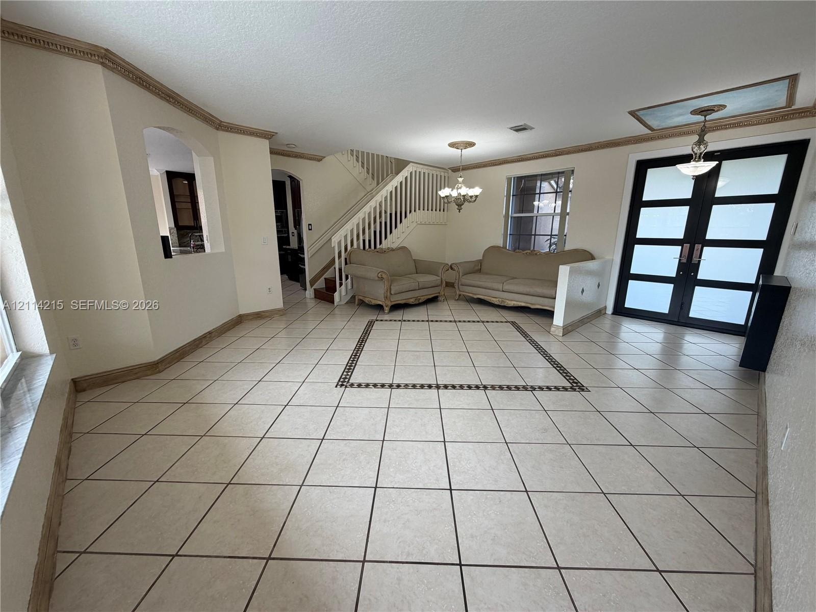 Interior space featuring diagonal tile flooring with decorative inlay, double-entry door with frosted glass panes, staircase with vertical balusters, 