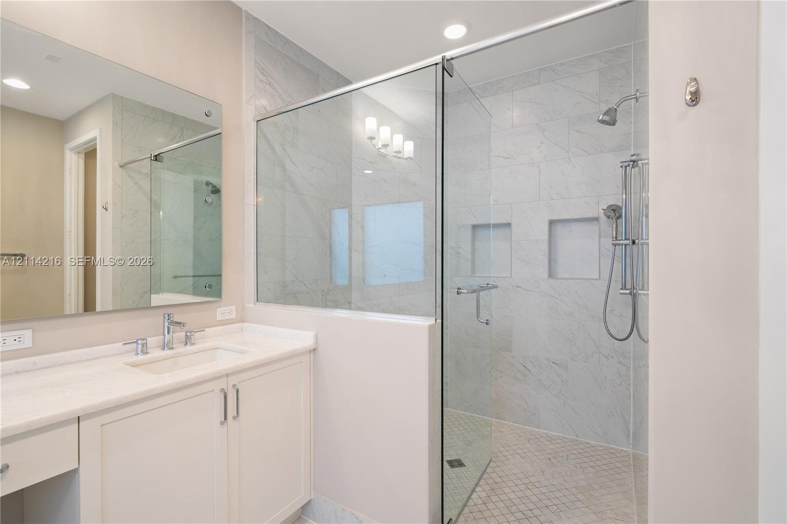Bathroom featuring a vanity with a light-toned countertop, undermount sink, and integrated cabinetry, paired with a walk-in shower enclosed by glass p