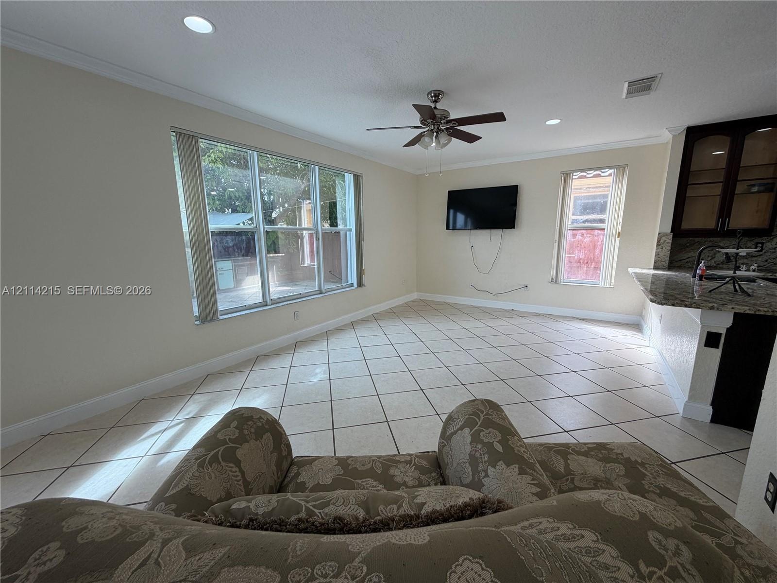 Open-concept space featuring large-format ceramic tile flooring, recessed lighting, ceiling fan, and crown molding