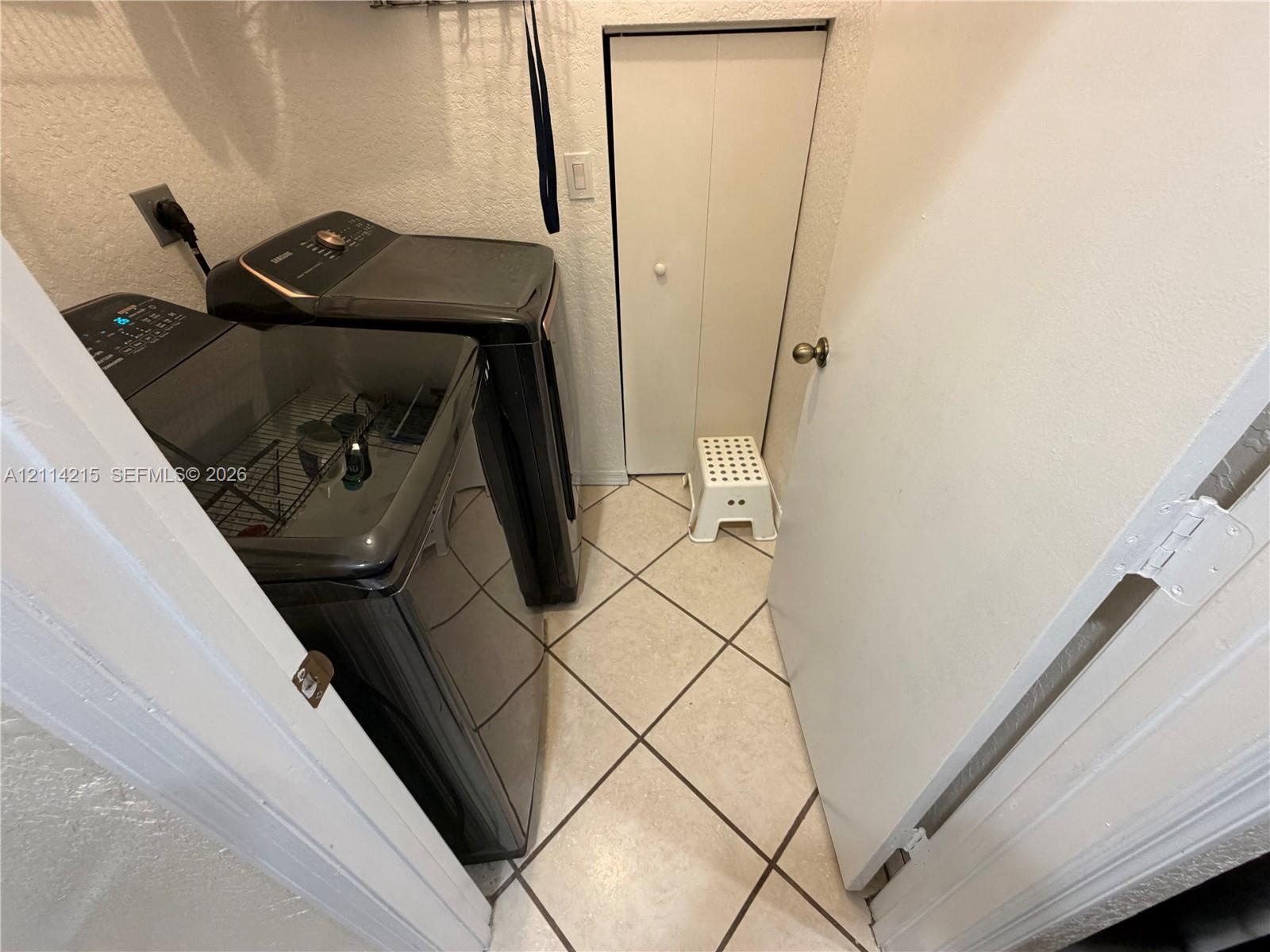 Laundry room featuring diagonal-set floor tile, textured wall finishes, and a bifold closet door