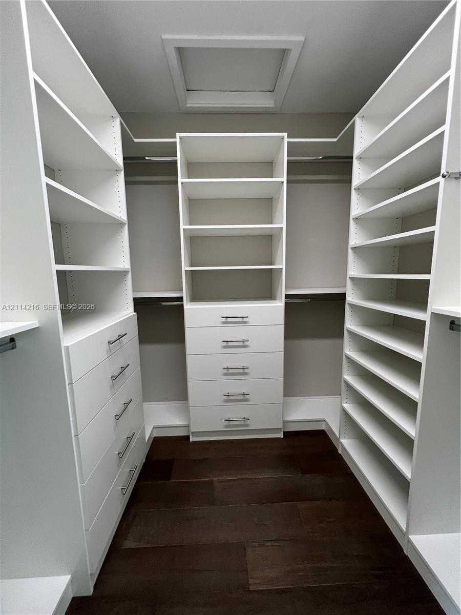 Custom walk-in closet featuring extensive white built-in shelving, multiple integrated storage drawers with brushed nickel hardware, and dark wood-fin