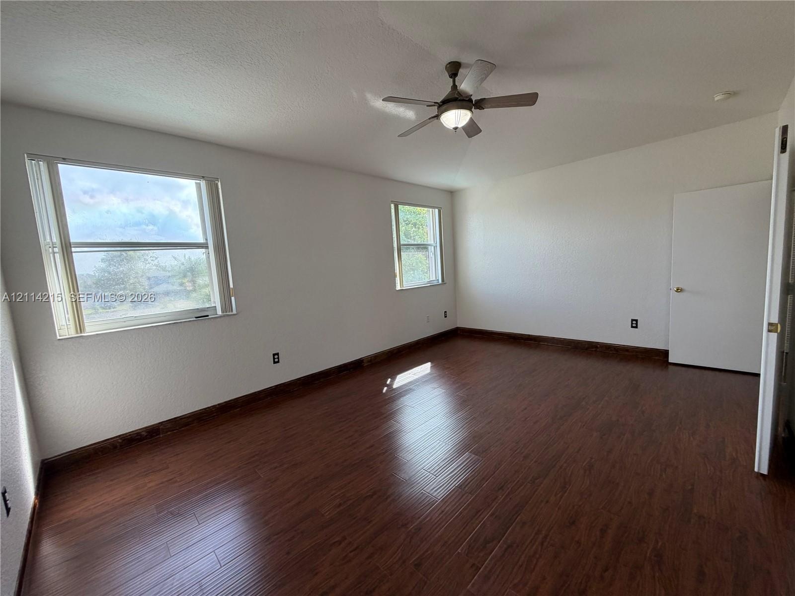Spacious room featuring wood-finish flooring, vaulted ceilings, a central ceiling fan with integrated lighting, and multiple windows