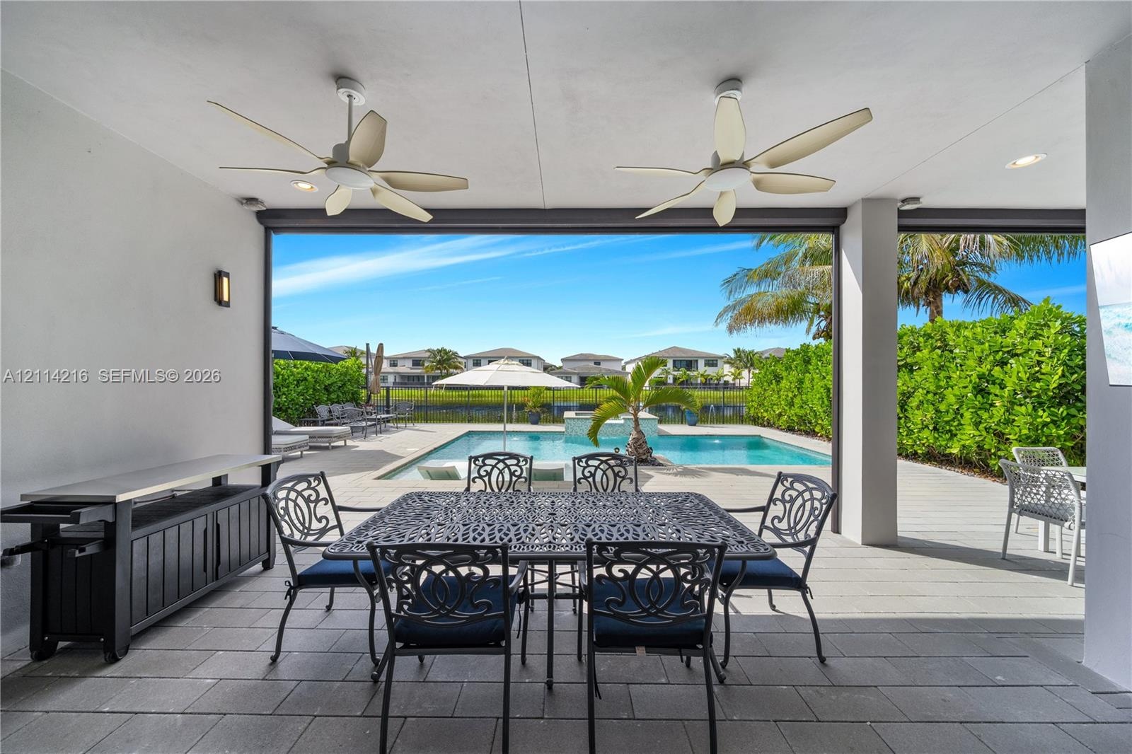 Covered patio featuring large-format tile flooring, dual ceiling fans, and recessed lighting, overlooking a private swimming pool with a stone water f
