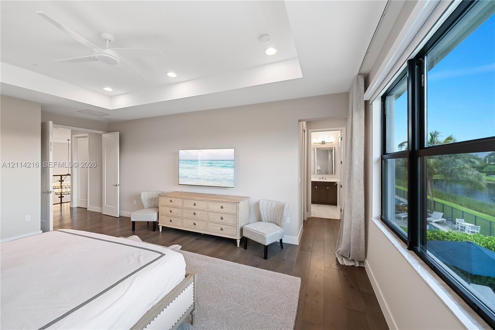 Tray ceiling, wood-finish flooring, ceiling fan, and large windows with exterior water scenery