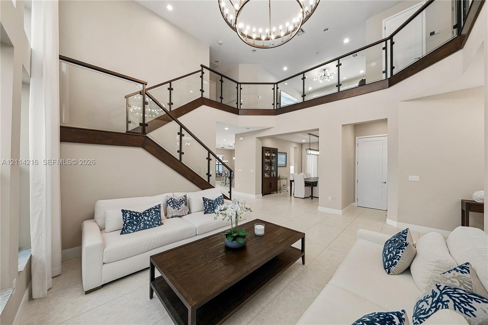Two-story foyer featuring high ceilings, open-concept balcony with glass railings, wood-cased staircase, circular tiered chandelier, and tile flooring
