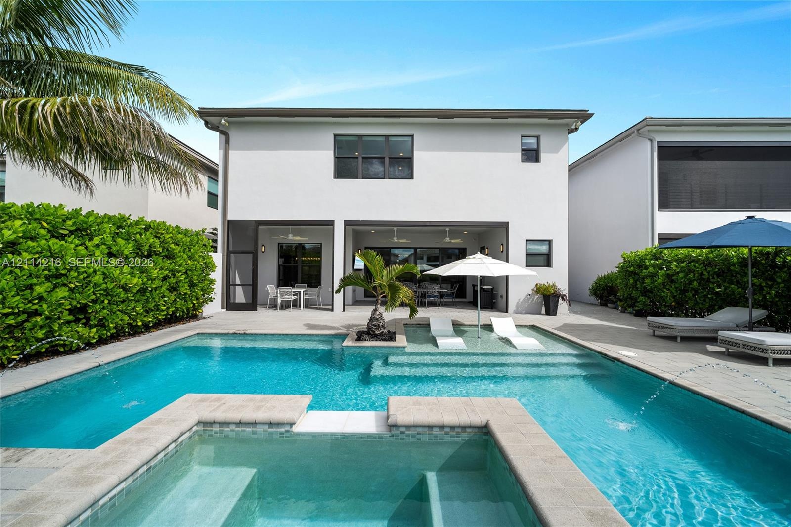 Swimming pool featuring a sun shelf with water fountains, raised spill-over spa, paved deck, and a covered lanai