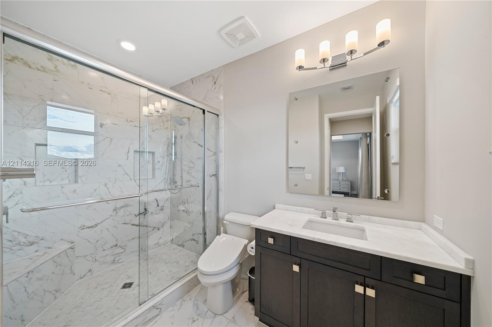 Bathroom featuring a glass-enclosed walk-in shower with stone-patterned tile, dark wood-finish cabinetry, a white countertop with an integrated rectan