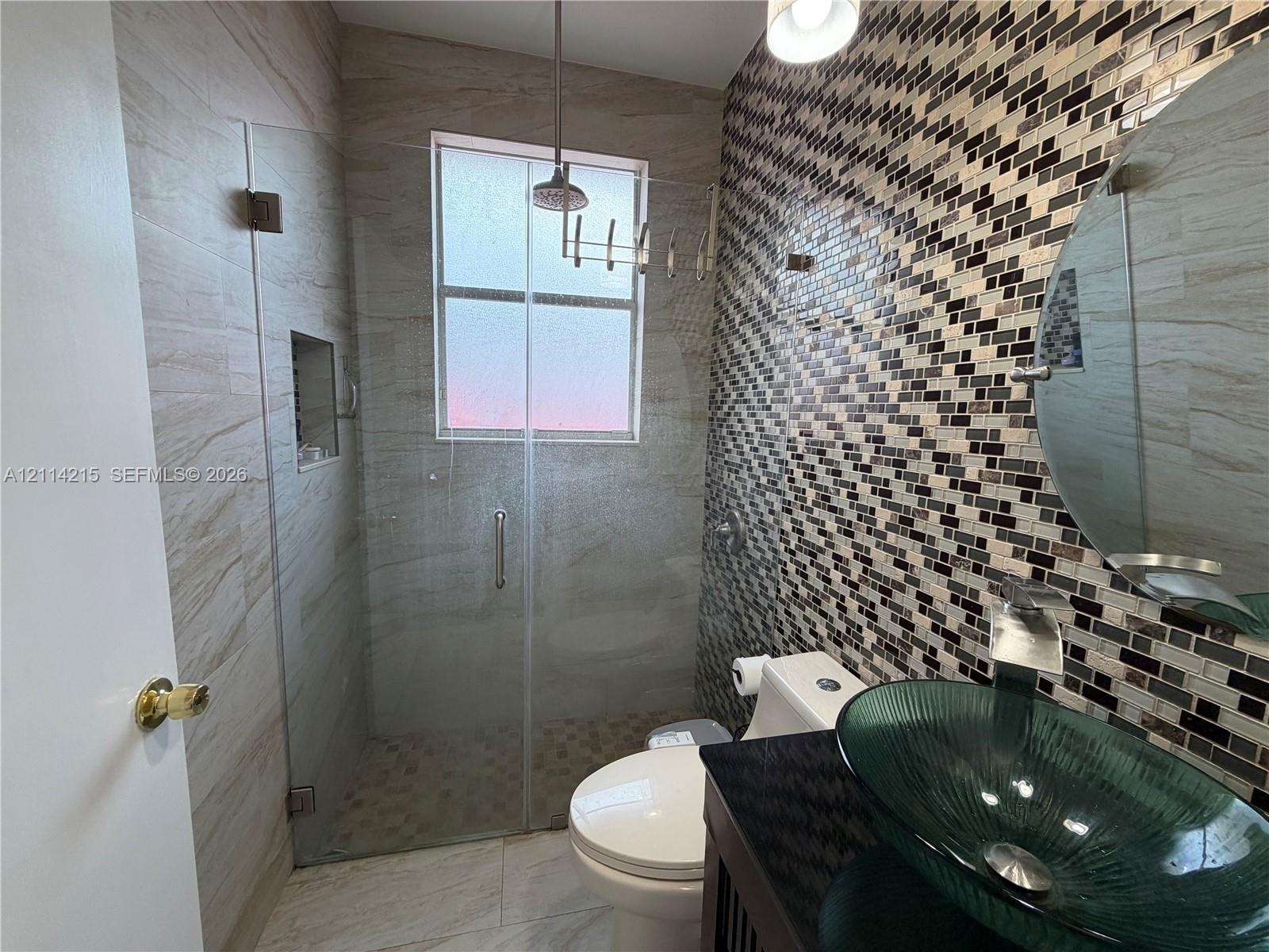 Bathroom featuring a glass vessel sink, dark stone countertop, mosaic tile accent wall, and a walk-in shower with a glass enclosure and recessed niche