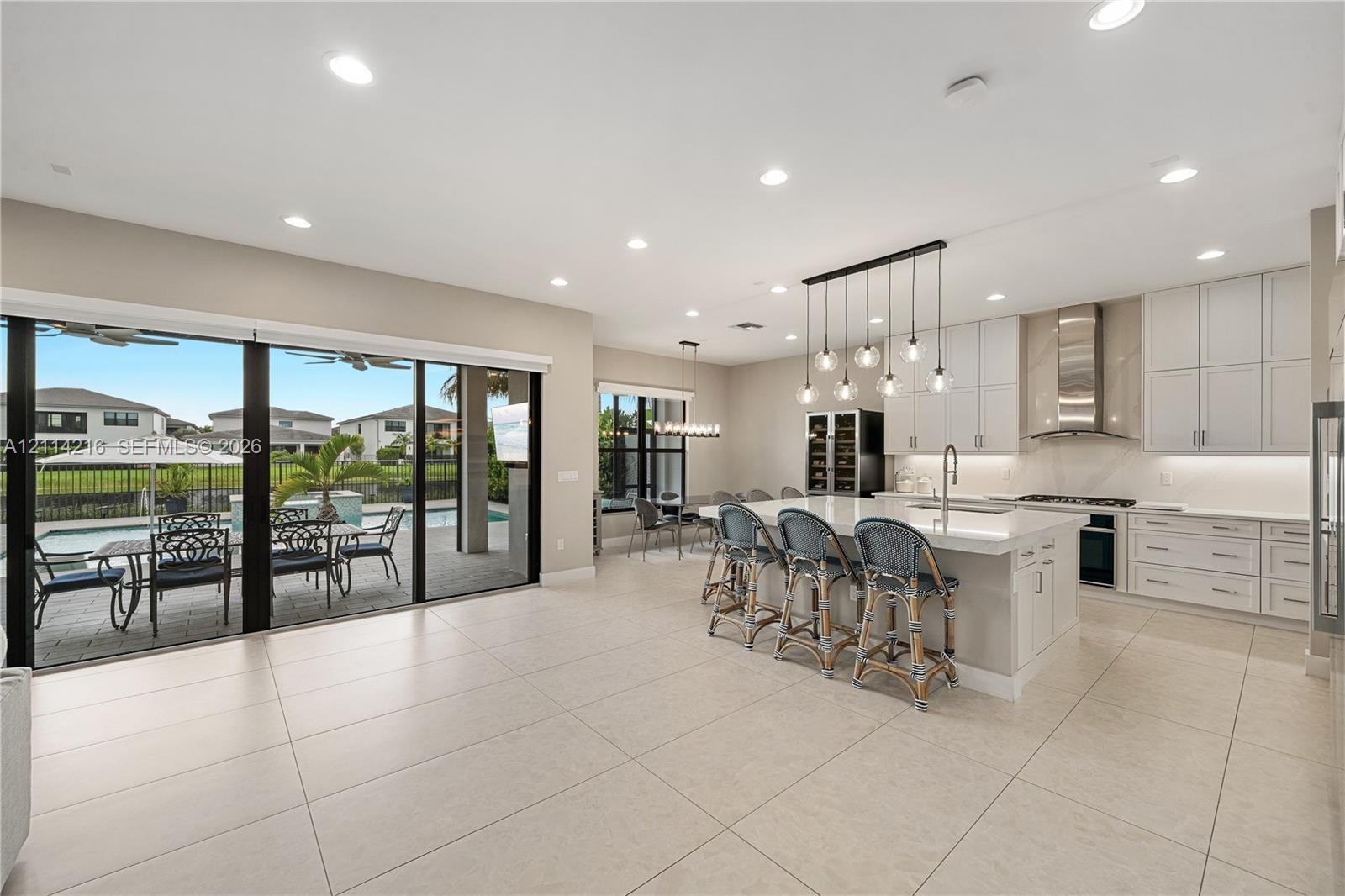 Kitchen featuring shaker-style cabinetry, quartz countertops, a stainless steel range hood, integrated wine storage, and oversized sliding glass doors