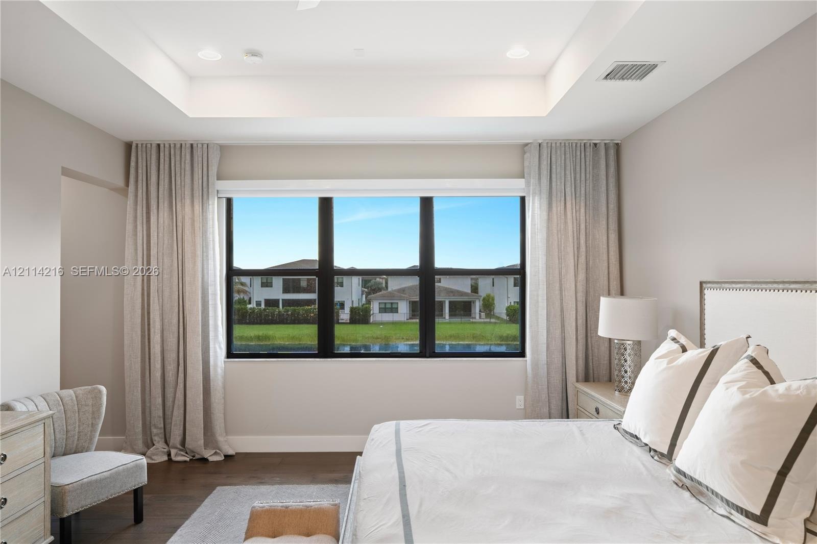 Tray ceiling with integrated recessed lighting and large windows featuring black frames and wood-finish flooring