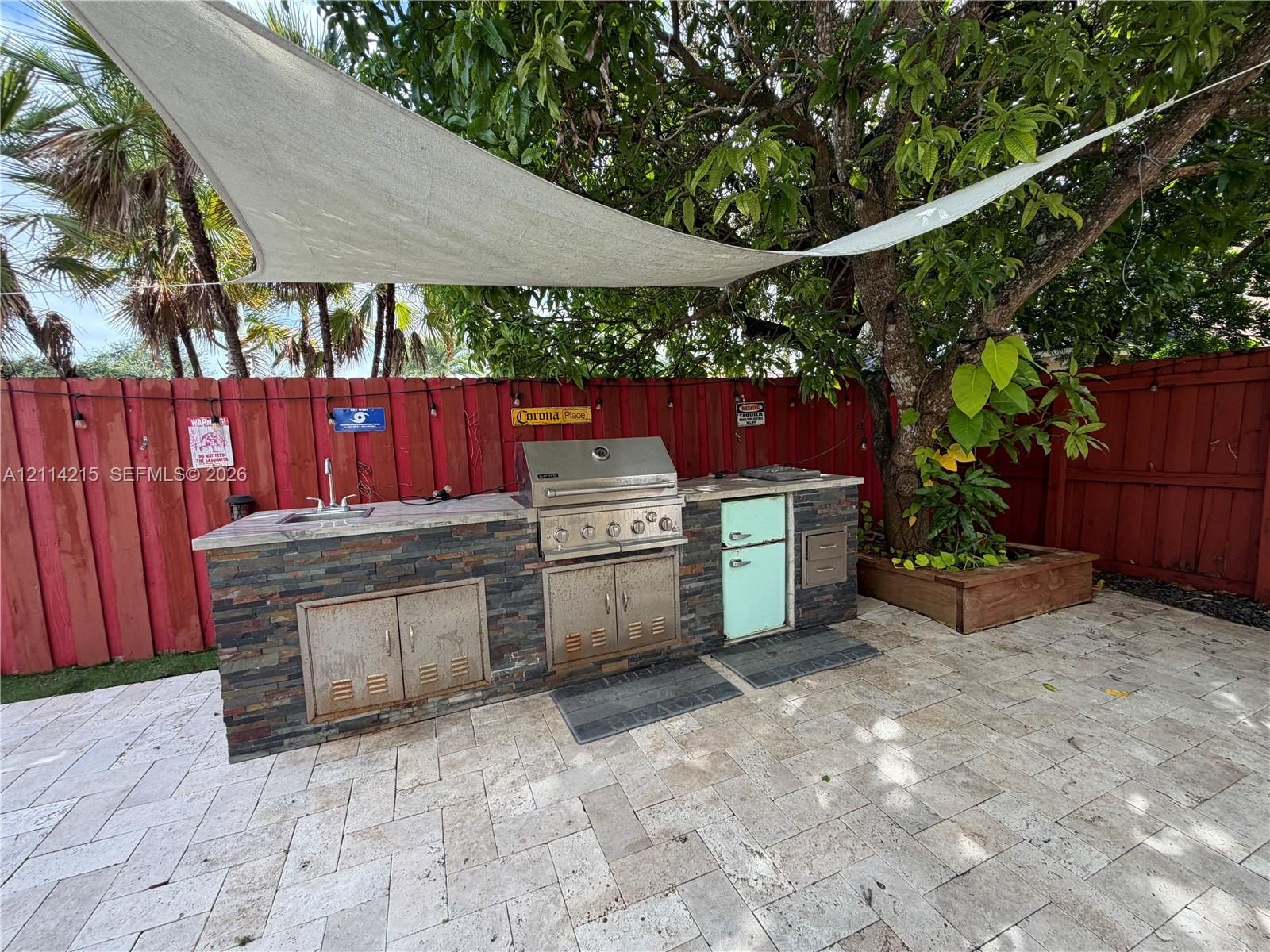Outdoor kitchen featuring a stacked stone exterior, integrated stainless steel grill, drop-in sink, and stone paver patio