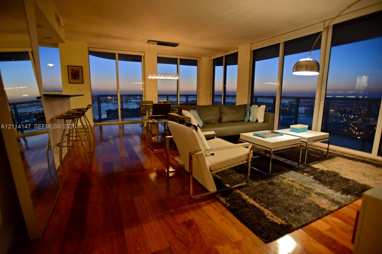 Open-concept living space featuring wood-finish flooring, floor-to-ceiling glass windows, and a built-in breakfast bar