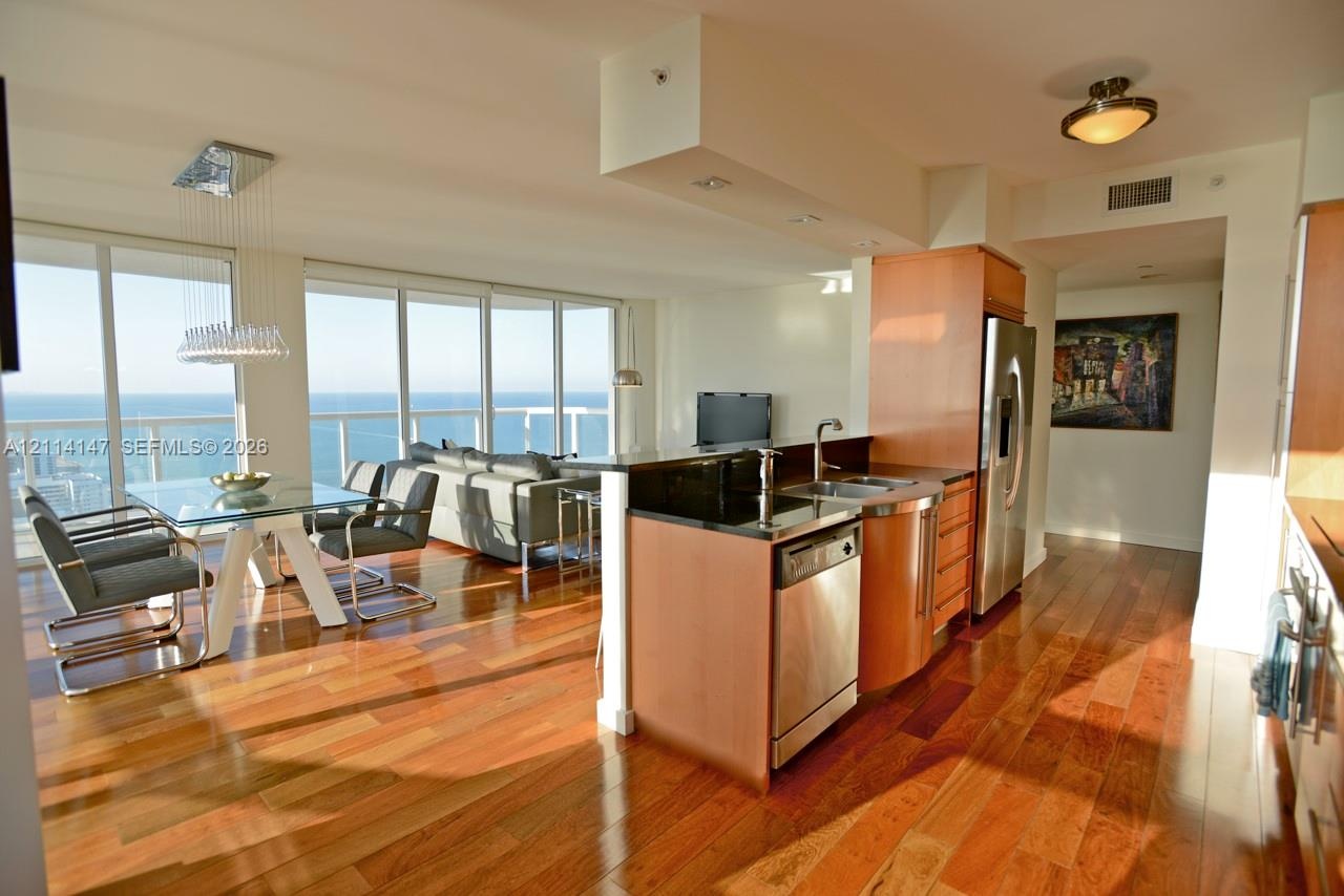 Wood-finish flooring, kitchen island with dark solid-surface countertop, stainless steel appliances, and floor-to-ceiling windows