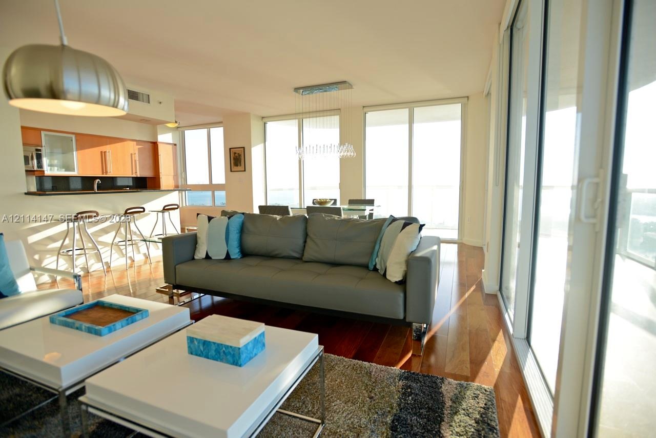 Open-concept floor plan featuring wood-finish flooring, floor-to-ceiling glass sliding doors, built-in cabinetry, and integrated pendant lighting