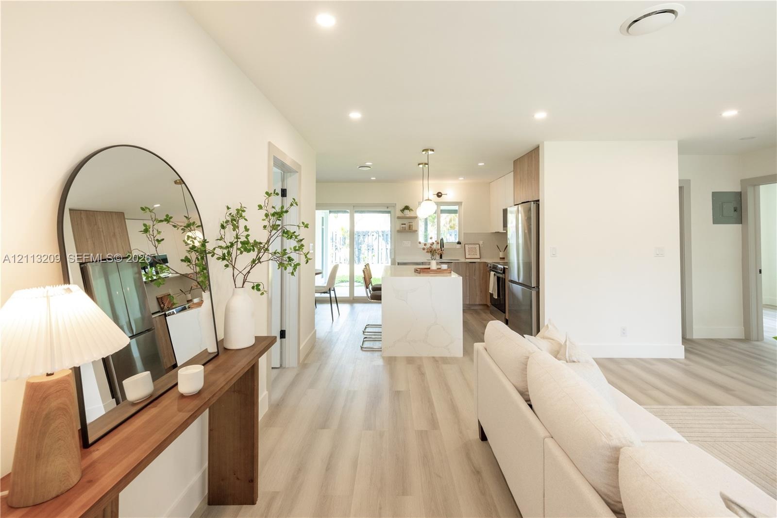 Open-concept interior featuring light wood-finish flooring, a kitchen island with stone-finish waterfall countertop, stainless steel appliances, and r