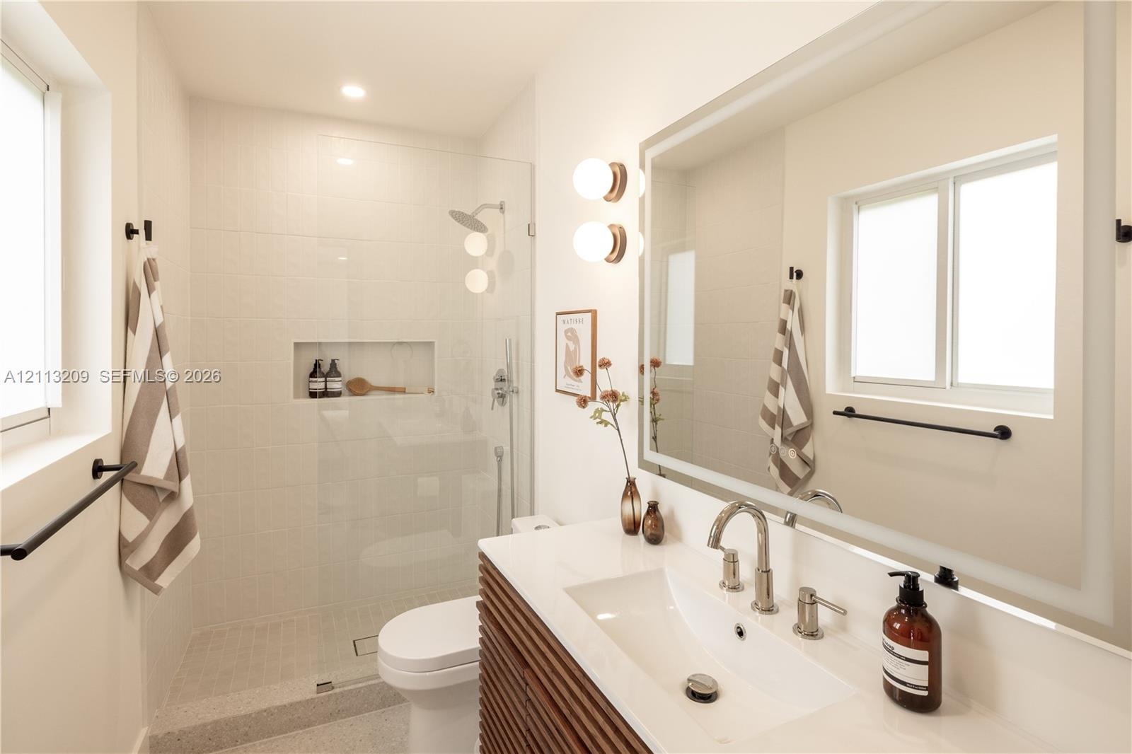 Bathroom featuring a slatted wood-finish vanity with a white countertop, walk-in shower with a glass enclosure and integrated wall niche, and a large 