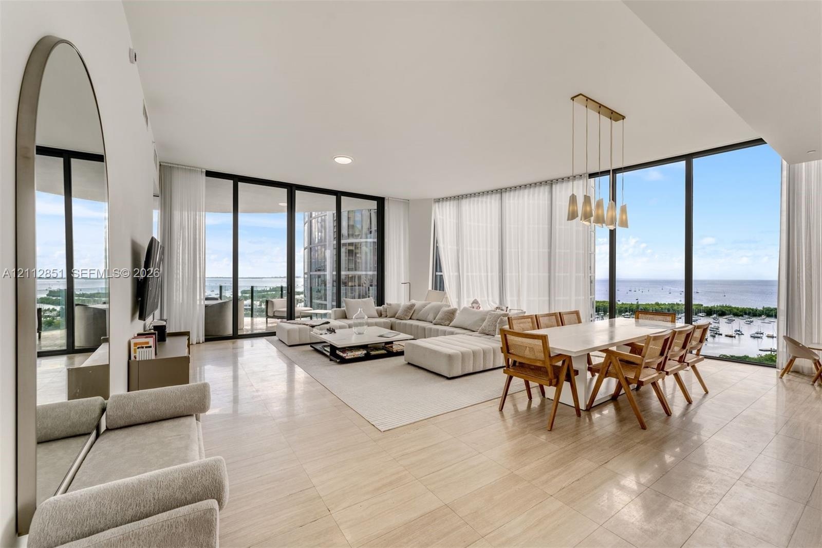 Open-concept living space featuring floor-to-ceiling glass walls, stone-finish tile flooring, and a multi-pendant light fixture