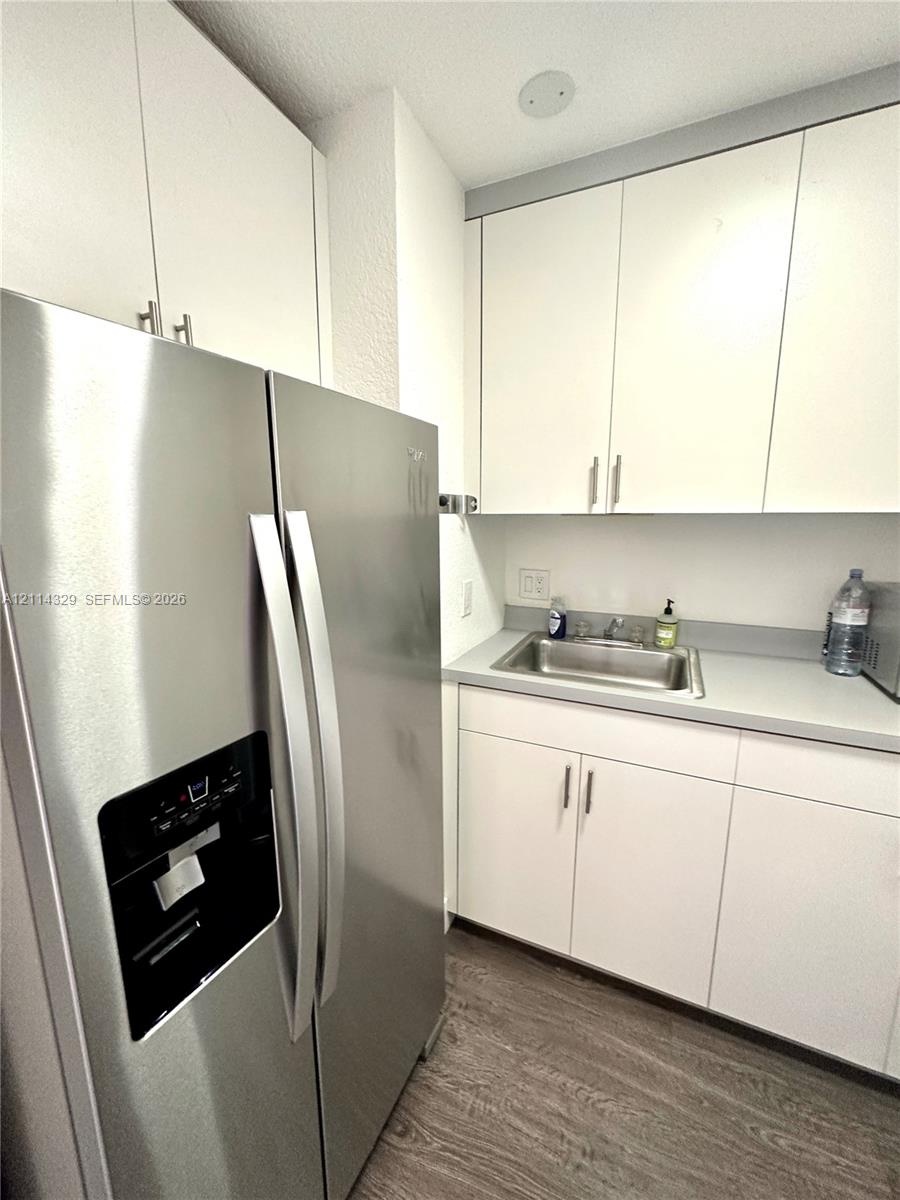 Stainless steel side-by-side refrigerator, white cabinetry with brushed metal hardware, solid-surface countertop, and integrated sink with faucet fixt