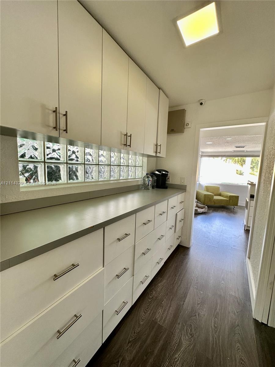 Custom cabinetry with matte metal pulls, solid-surface countertops, glass block backsplash, and wood-finish flooring