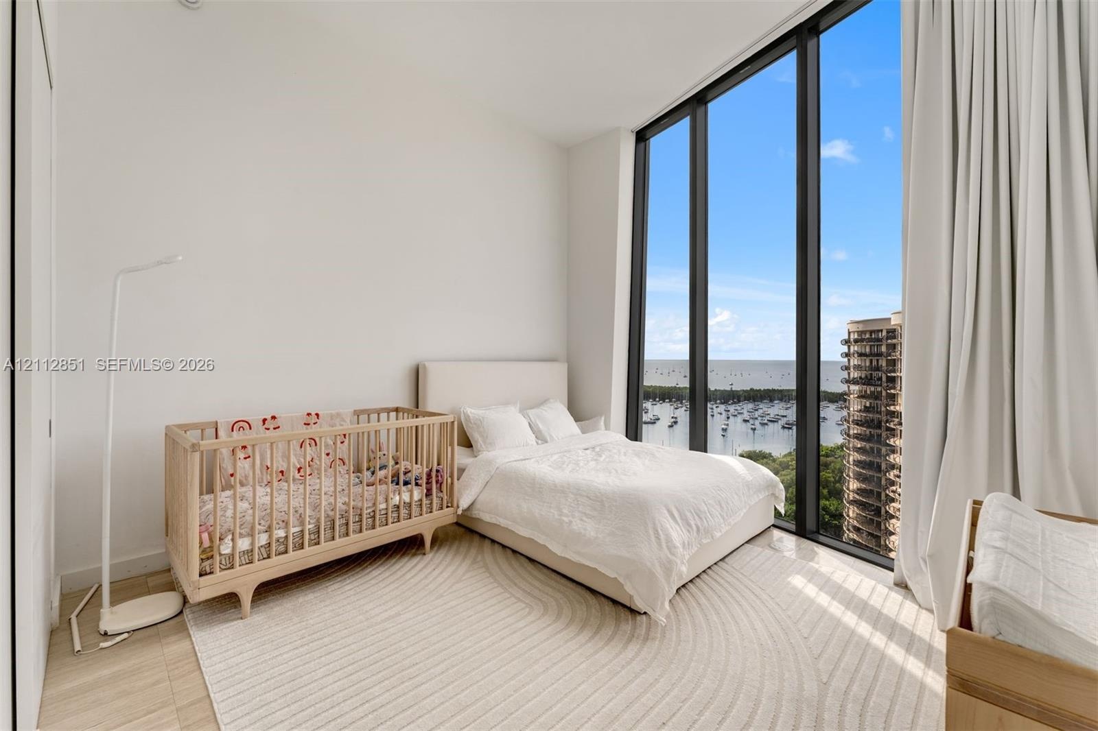 Floor-to-ceiling windows featuring expansive coastal and marina scenery, complemented by light-toned wood-finish flooring