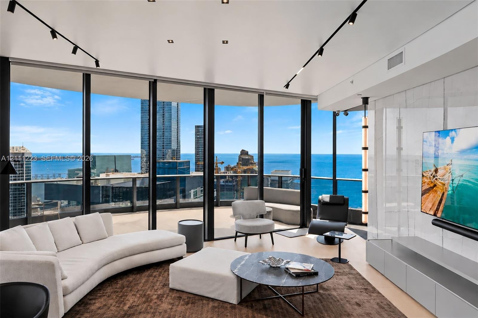 Floor-to-ceiling windows featuring panoramic water and city scenery, expansive curved balcony, stone-finish accent wall with integrated media cabinetr