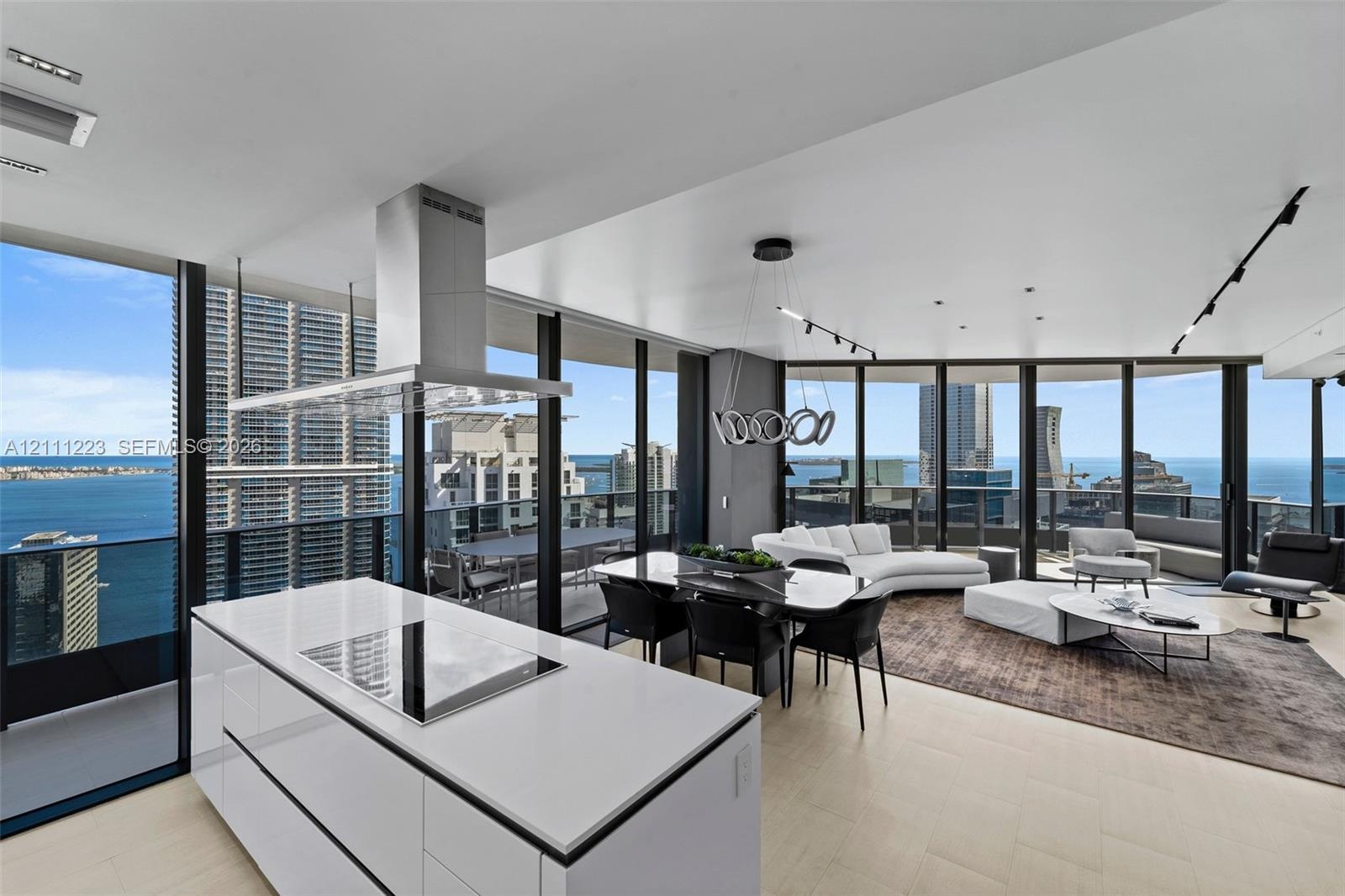 Open-concept kitchen featuring a white center island with a built-in cooktop, stainless steel range hood, floor-to-ceiling windows, light-toned floori