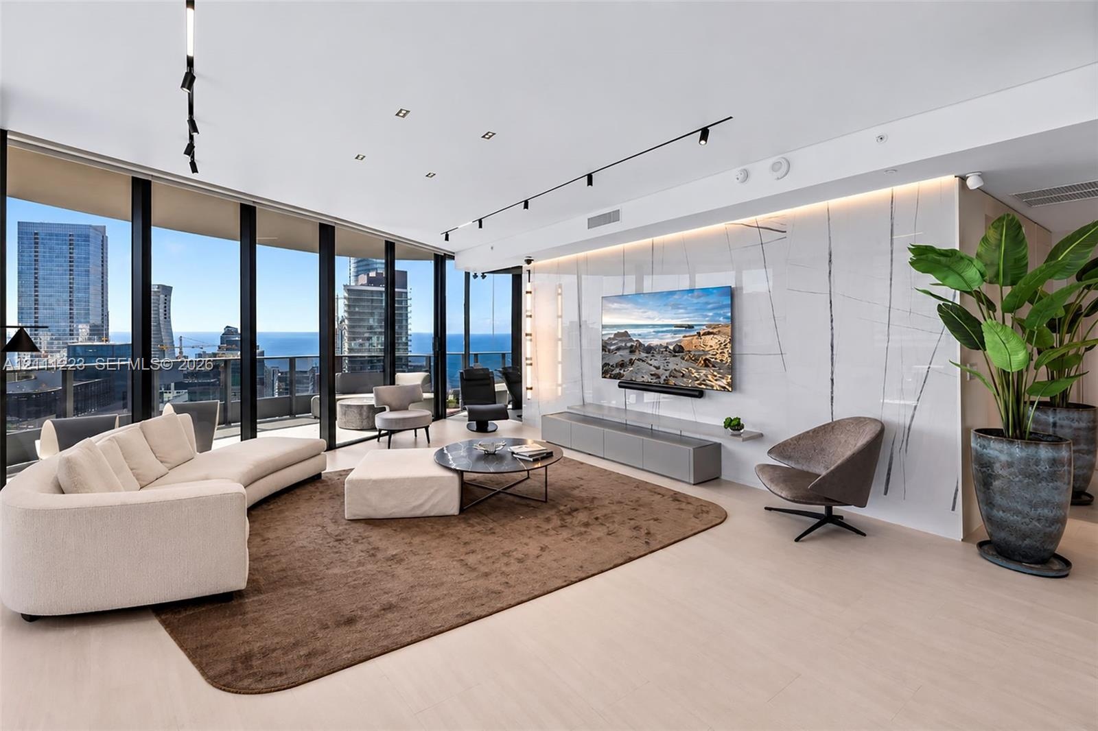 Floor-to-ceiling windows featuring panoramic city and water scenery, light-toned wood-finish flooring, large-format stone feature wall with integrated