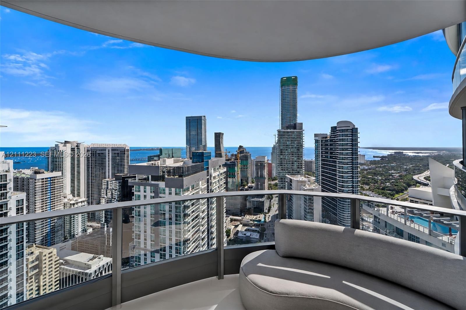 Covered balcony with a curved structural layout, featuring a glass-panel railing and panoramic urban and water scenery