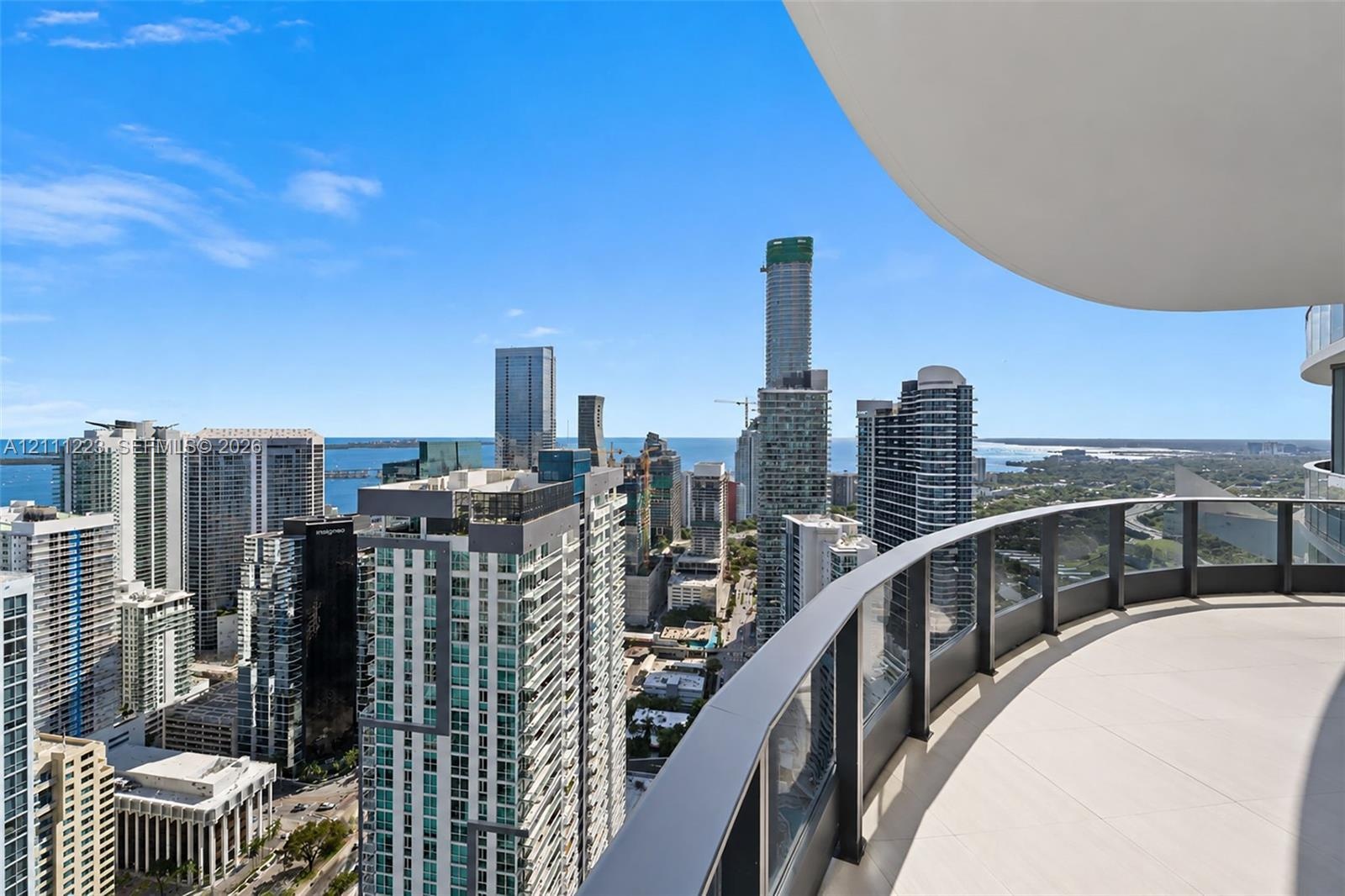 Curved balcony featuring light-colored tile flooring and a glass-paneled railing overlooking an expansive cityscape and water horizon