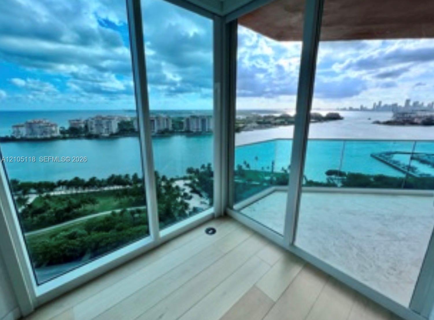 Floor-to-ceiling windows, wood-finish flooring, and a glass-paneled balcony overlooking the water and city skyline