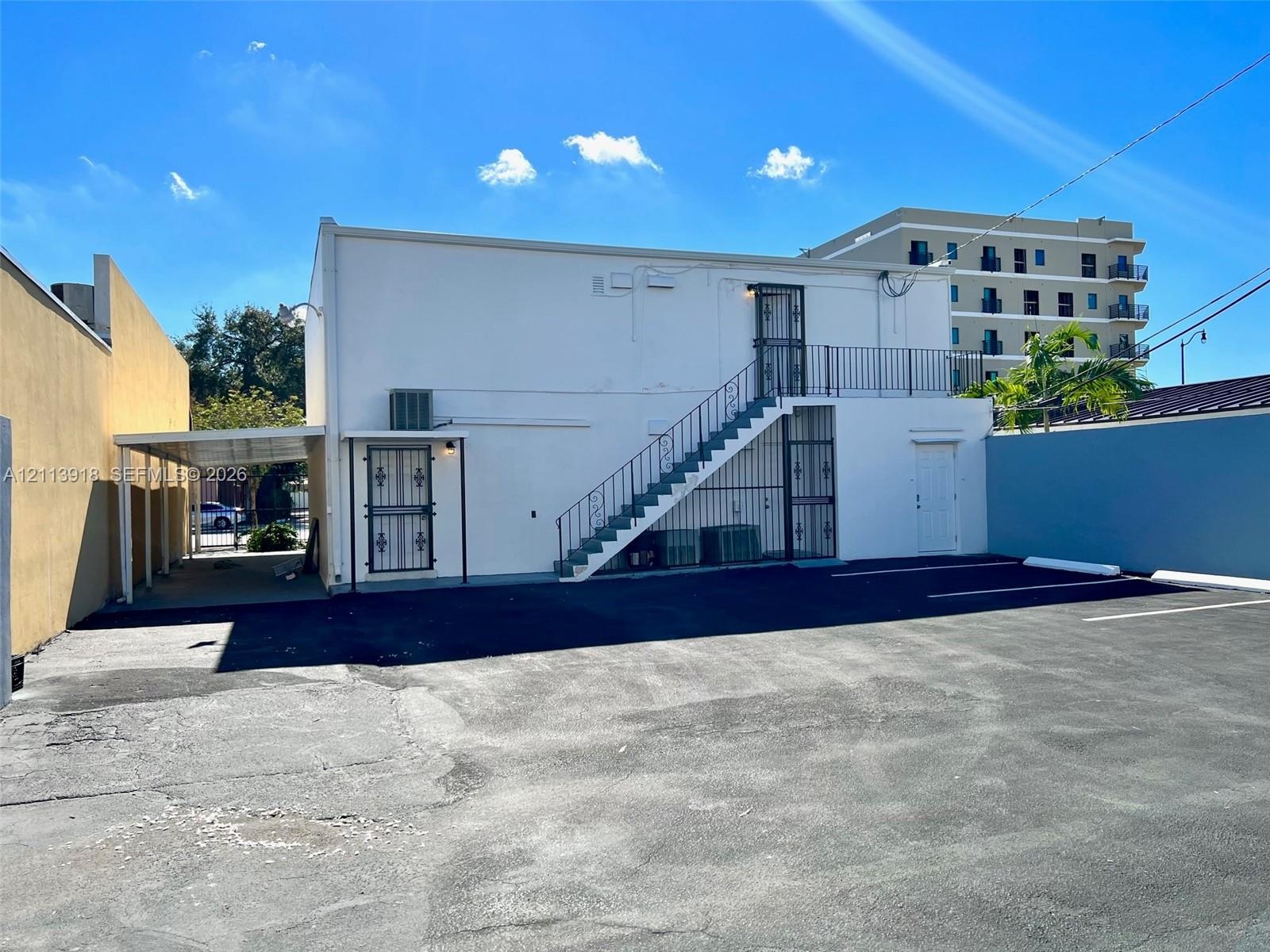 Exterior featuring a paved parking area, covered carport, and metal staircase with iron railings