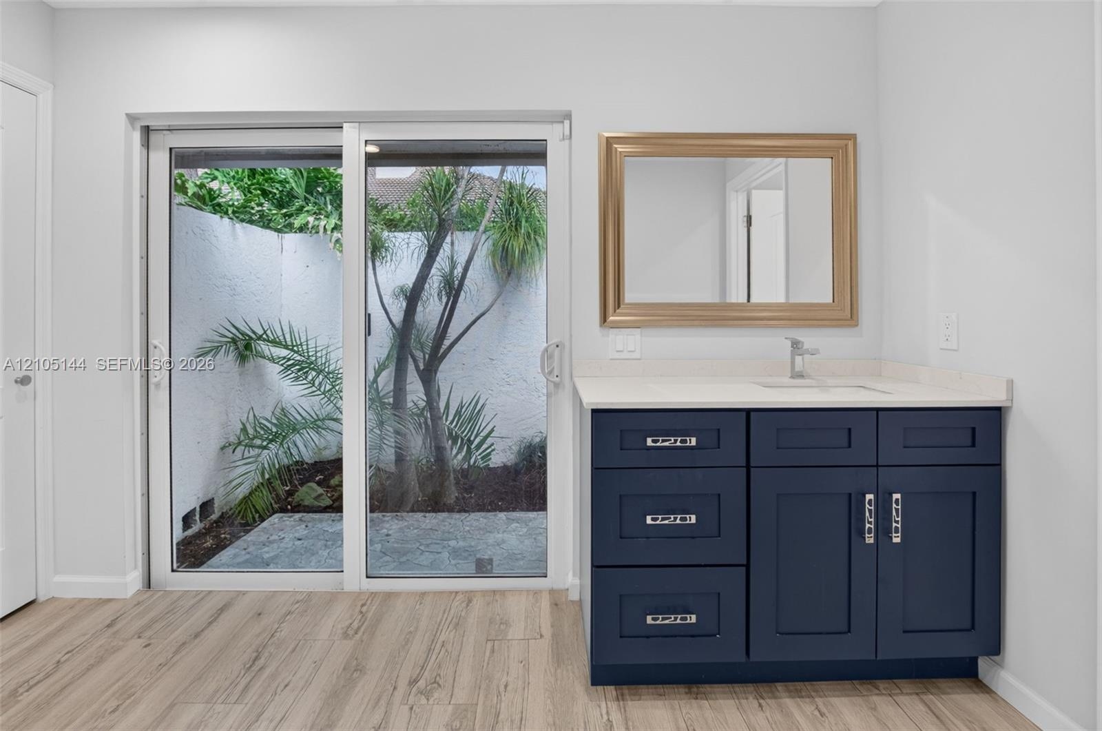 Dark blue shaker-style vanity with a light-toned countertop, integrated basin, silver-finish hardware, and wood-finish flooring, featuring sliding gla