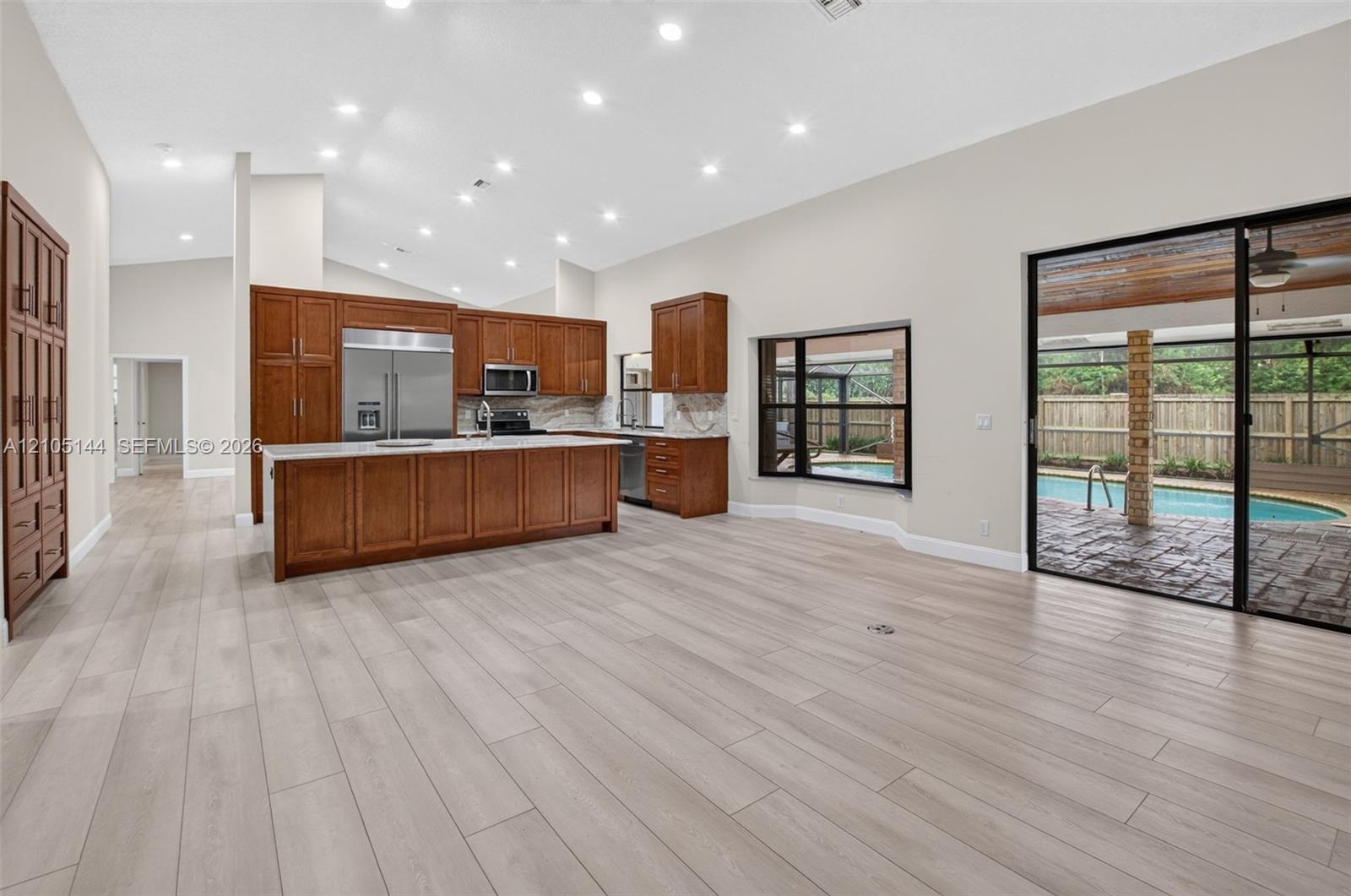 Kitchen featuring stained wood cabinetry, stainless steel appliances, and a center island with light-toned countertops, complemented by wood-finish fl