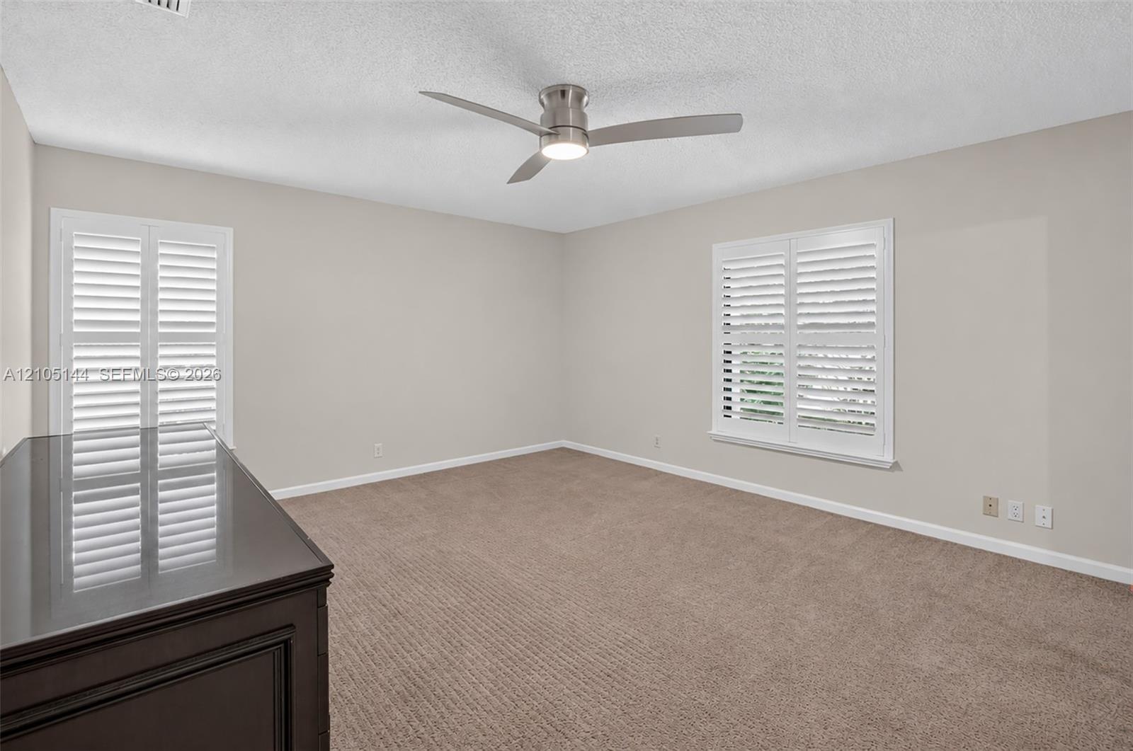 (FAN VIRTUALLY STAGED AS SIMILAR PIECE WILL BE INSTALLED) Neutral-toned interior featuring wall-to-wall carpeting, white plantation shutters, and a mo