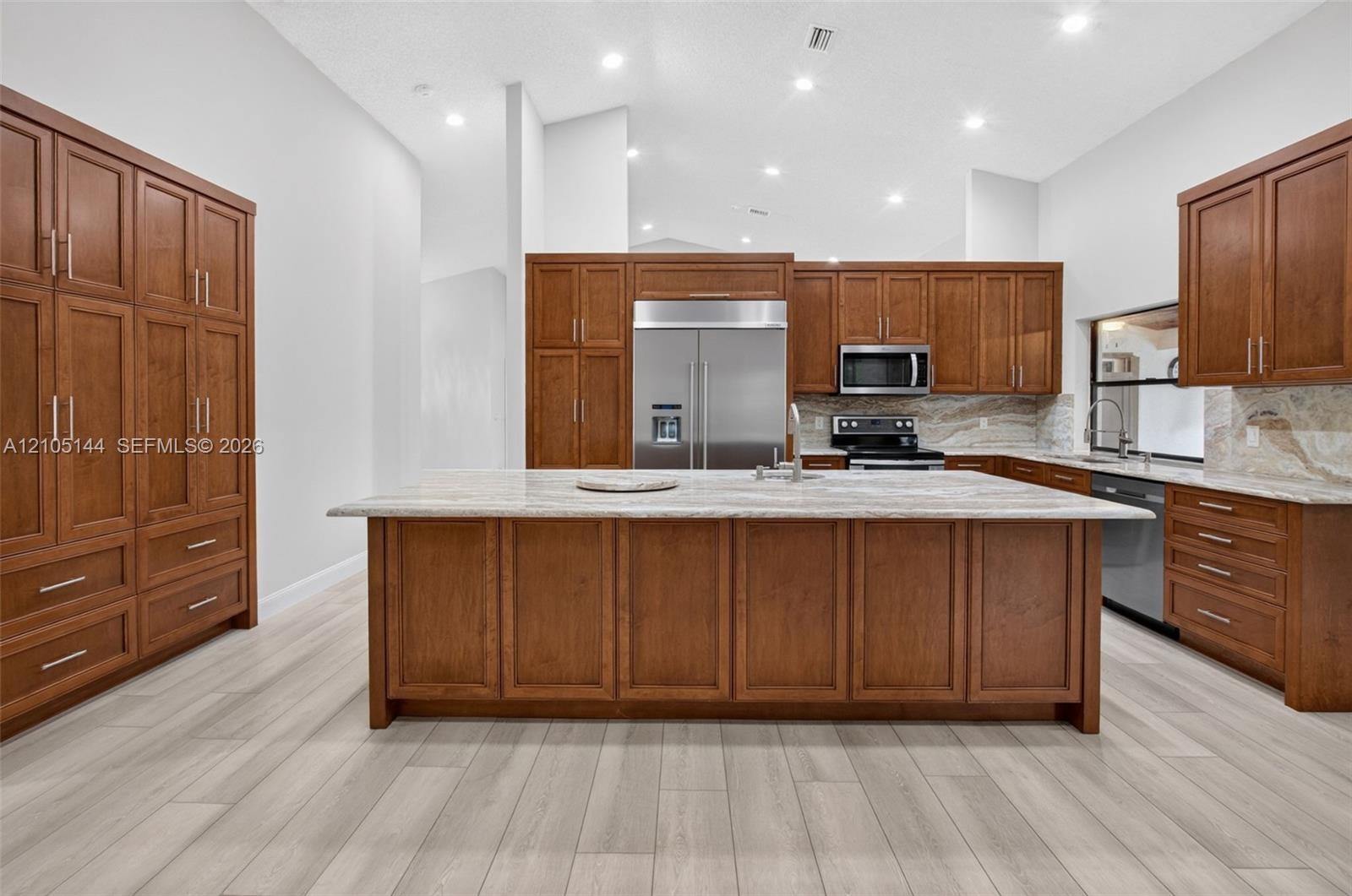 Kitchen featuring custom wood cabinetry, central island with stone countertop, stainless steel appliances, and wood-finish flooring under recessed lig